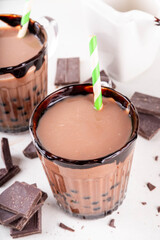 Tasty hot chocolate bubble tea. Cocoa hot or cold beverage with with tapioca balls and dark chocolate syrup, sweet dessert drink on white table with crushed chocolate 