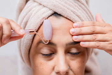 Woman using rose quartz jade roller on forehead