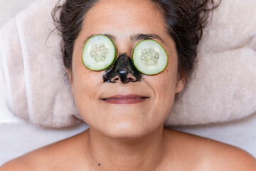 Relaxed woman enjoying spa facial treatment with cucumbers