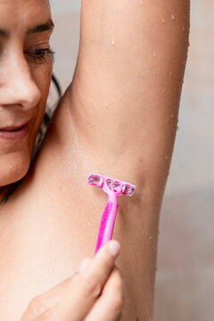Woman shaving her armpit with a pink razor