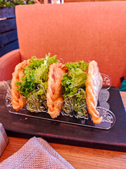 Crispy fried chebureki, traditional Eastern European meat turnovers, served with fresh lettuce in a metal holder on a wooden table in a cozy restaurant setting.