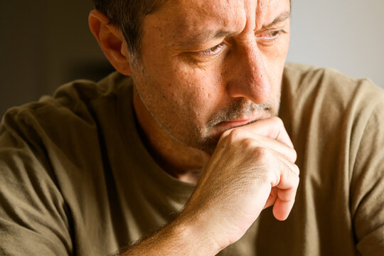 Indoor portrait of a pensive man resting his chin on his hand, thoughtful expression symbolizing contemplation, decision making, and introspection.