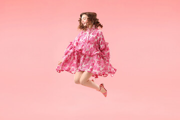 Beautifully dressed young woman jumping on pink background