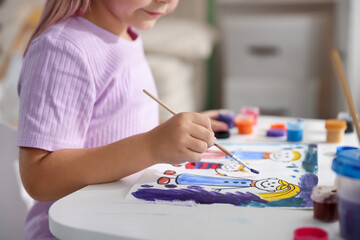 Little girl with brush drawing at white table indoors, closeup