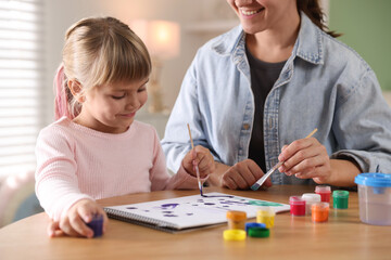 Mother and her little daughter drawing together at wooden table indoors, closeup