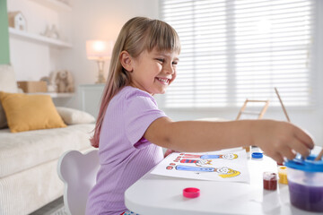 Little girl with brush drawing at white table indoors