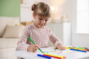 Cute little girl drawing with felt pen at white table indoors