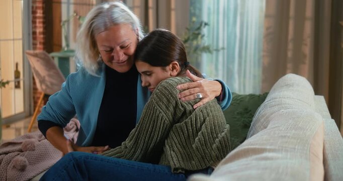 Grandmother warmly hugging her teenage granddaughter after a disagreement, smiling and sharing a heartfelt moment of reconciliation and family affection at home.