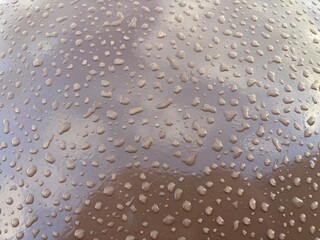 The glossy brown surface is covered with numerous water drops, creating a dynamic and material visual effect.