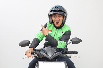 Asian online taxi driver, male motorbiker wearing jacket and helmet, pointing back at empty space, isolated on white background.