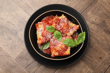 Delicious ravioli with tomato sauce, cheese and basil on wooden table, top view