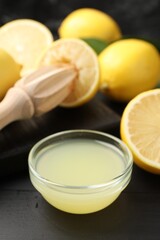 Fresh lemon juice, fruits and squeezer on black wooden table, closeup