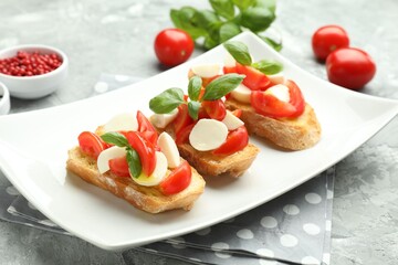 Tasty bruschettas with mozzarella cheese, tomatoes, basil and spices on grey textured table, closeup