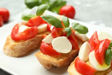 Tasty bruschettas with mozzarella cheese, tomatoes and basil on grey table, closeup