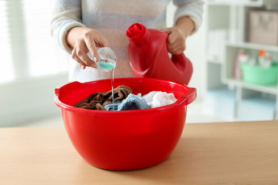 Woman pouring detergent into plastic basin with towels at wooden table indoors, closeup - Powered by Adobe