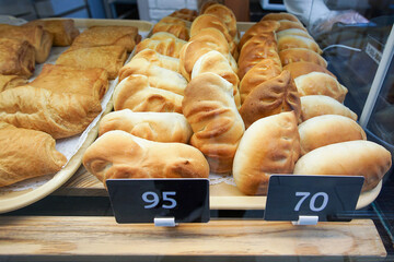 Freshly baked buns and pies made from wheat bread are on display for sale on a shelf in the store.