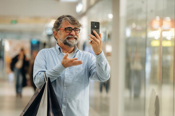 Video call, using smartphone. Senior man is in the mall, shopping time conception
