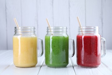 Different tasty smoothies in mason jars on white wooden table