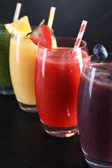 Different tasty smoothies in glasses with ingredients on black wooden table, closeup