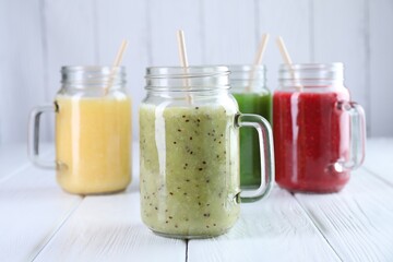 Different tasty smoothies in mason jars on white wooden table