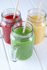 Different tasty smoothies in mason jars on white wooden table