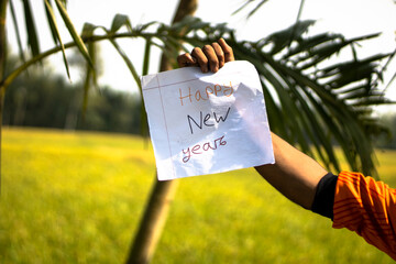 Hand holding a paper with happy new year message in outdoor setting