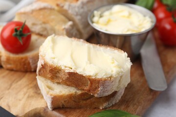 Cut baguette with butter, basil, tomatoes and knife on light table, closeup