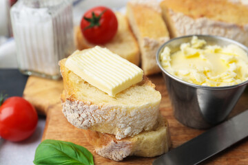 Cut baguette with butter, basil, tomatoes and knife on light table, closeup