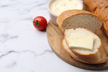 Slices of baguette with butter and tomato on white marble table, closeup. Space for text