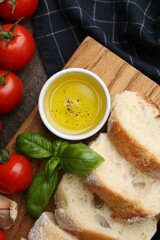 Tasty baguette served with oil, tomatoes and basil on wooden table, flat lay