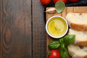 Tasty baguette served with oil, tomatoes and basil on wooden table, flat lay. Space for text
