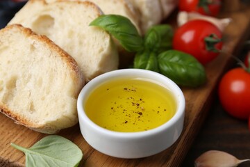Tasty baguette served with oil, tomatoes and basil on wooden table, closeup