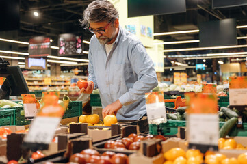 Vegetables section. A senior man is buying food in the grocery store