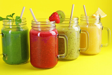 Different tasty smoothies in mason jars on yellow background, closeup