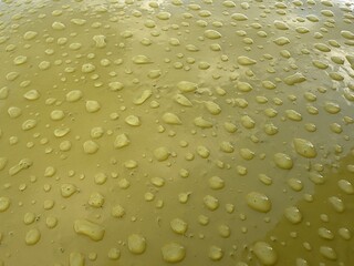 The glossy yellow surface is covered with numerous water drops, creating a dynamic and material visual effect.