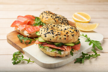 Delicious bagels with salmon, cream cheese, cucumber and arugula on wooden table, closeup