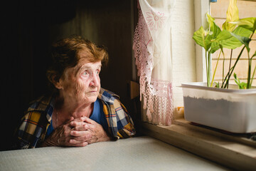 A gentle portrait of an elderly woman sitting by the window, hands folded, gazing outside with a soft, thoughtful expression as daylight filters through lace curtains.