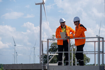 Workers in bright jackets discuss plans at a wind farm with turbines in the background under a sunny sky © Freeday photo