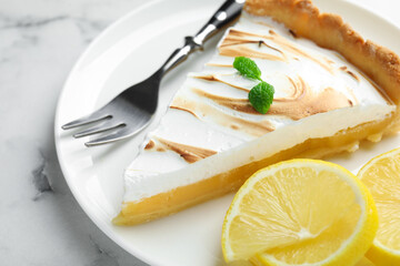 Slice of tasty lemon meringue tart with mint served on white marble table, closeup