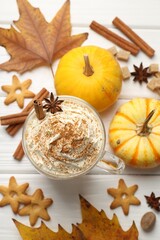 Tasty pumpkin latte with whipped cream in glass cup, cookies and ingredients on white wooden table, flat lay