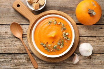 Tasty pumpkin cream soup with seeds served on wooden table, flat lay