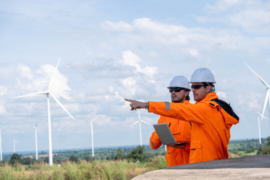 Engineers evaluate wind farm site while discussing data and future plans under a cloudy sky