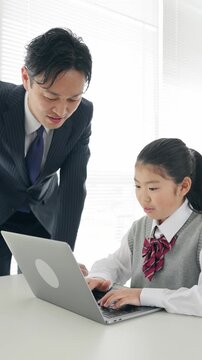 女の子にパソコンの使い方を指導する男性教師