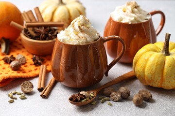 Tasty pumpkin latte with whipped cream in cups, spices and ingredients on light grey table, closeup