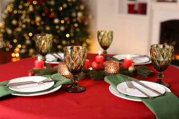 Stylish Christmas table setting with plates, glasses and burning candles in festive decorated room, closeup. Bokeh effect