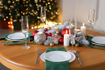 Stylish Christmas table setting with plates, glasses and burning candles in festive decorated room, closeup. Bokeh effect