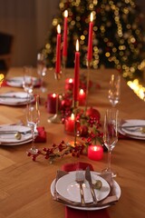 Stylish Christmas table setting with plates, glasses and burning candles in festive decorated room, closeup. Bokeh effect