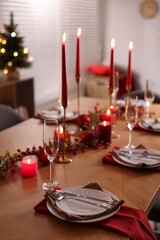 Stylish Christmas table setting with plates, glasses and burning candles in room, closeup. Bokeh effect