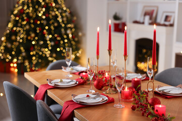 Stylish Christmas table setting with plates, glasses and burning candles in festive decorated room, closeup
