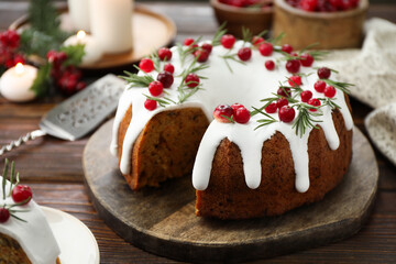 Delicious cut Christmas cake with icing, cranberries and rosemary on wooden table, closeup